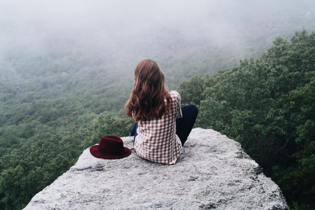 woman sitting on a mountain overlooking the fields embracing the 'i don't knows'