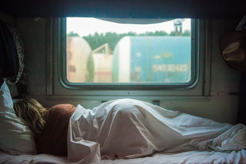 Blonde woman sleeping in pink sheet bed next to window in daytime