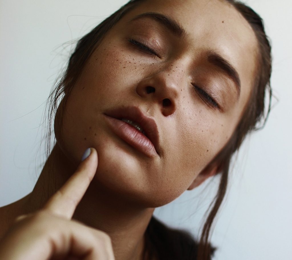 girl with freckles pointing at her chin