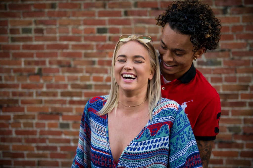 happy couple standing in front of brick wall, fall hard