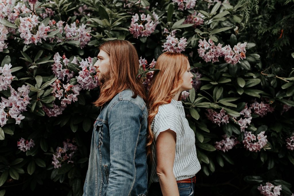 couple standing back to back in front of flowers