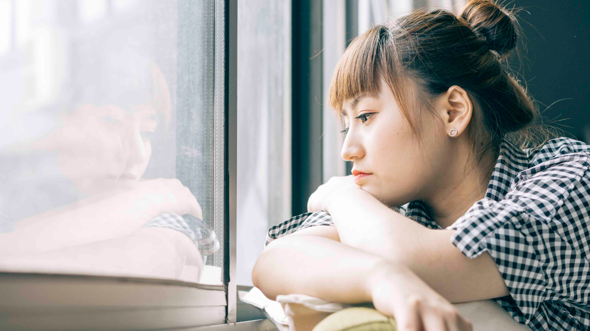 sad woman looking out the window missing home